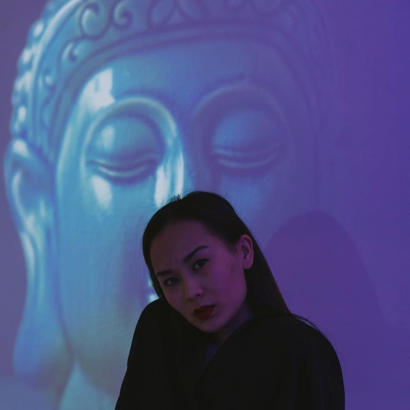 Woman in a serene yoga pose against a dark background with azure light.